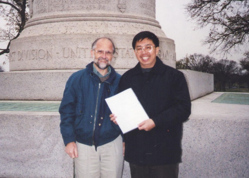 Photo of Nigel and Zhengjie in front of a monument holding a document.