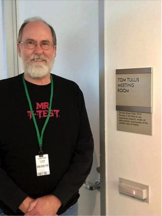 Picture of Tom Tullis standing in front of the meeting room named after him.