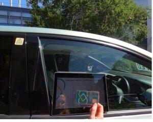 Photo of the outside car window with an embedded touchless device and a user  waving a card